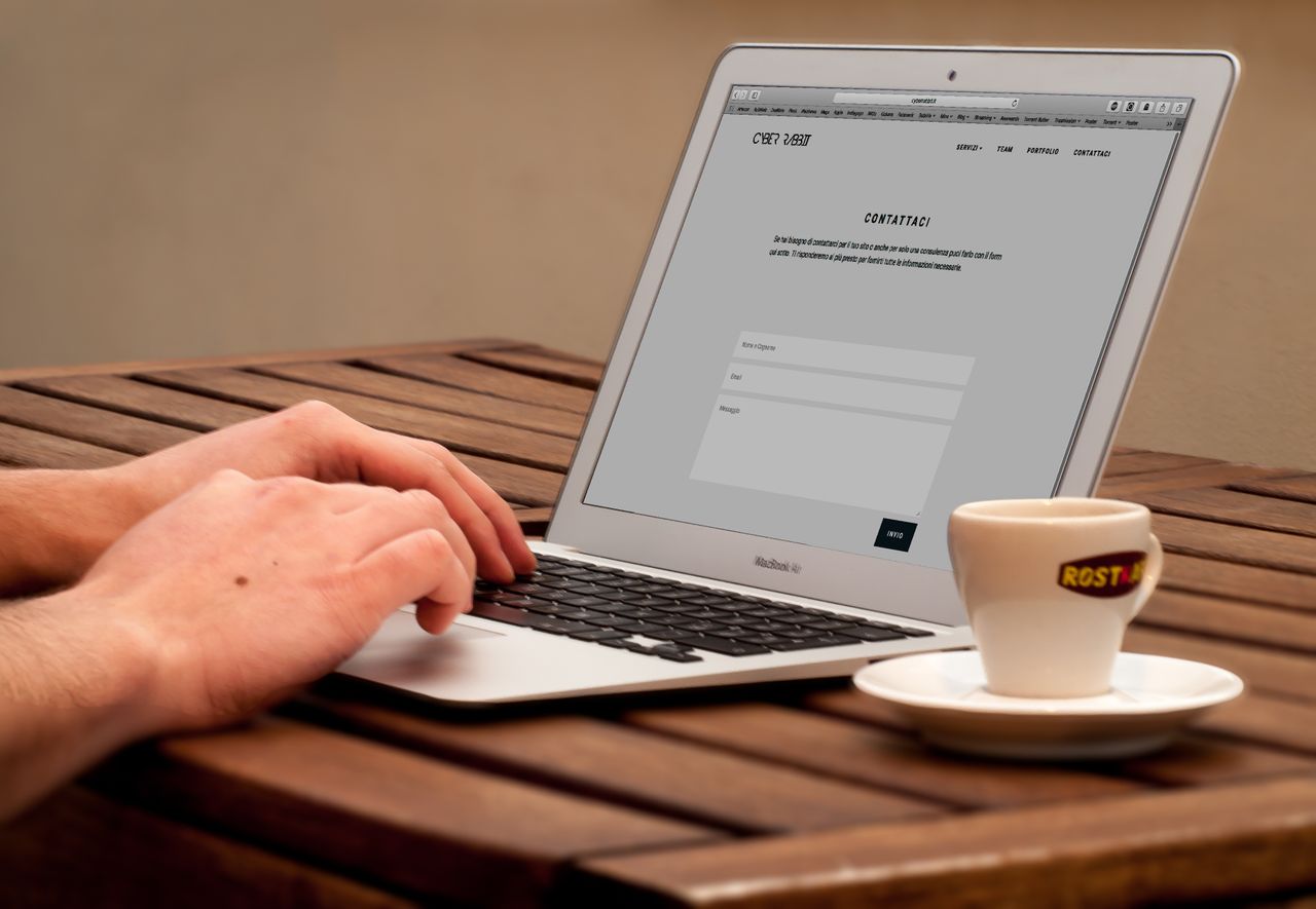 Gros plan sur des mains tapant sur un ordinateur portable, à côté d'une tasse de café, sur un bureau en bois.